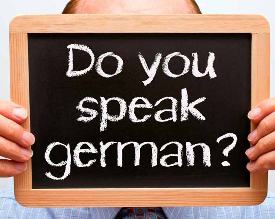 Mann hält eine kleine Tafel vor seinem Gesicht, auf der mit Kreide geschrieben steht: "Do you speak german?"