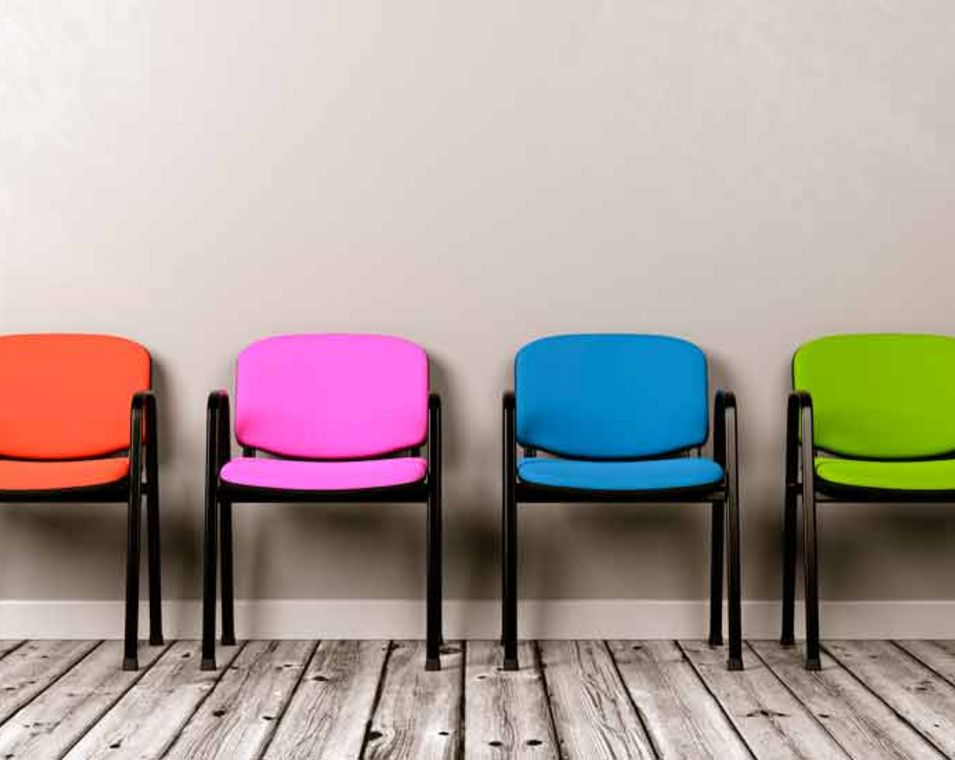 Vier verschiedenfarbige Stühle stehen nebeneinander an einer Wand