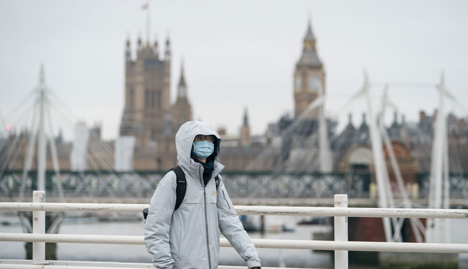 Mann mit Maske überquert die Waterloo Bridge in London, im Hintergrund sieht man den Big Ben. 