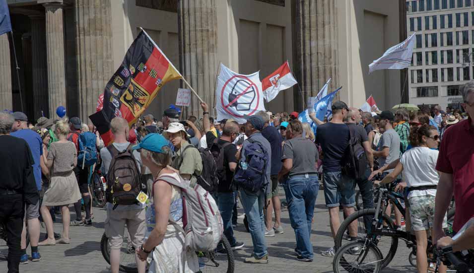 Gemischte Gruppe an Teilnehmenden einer Demonstration gegen Corona-Maßnahmen mit Schildern und Fahnen Ende Juli 2022 in Berlin