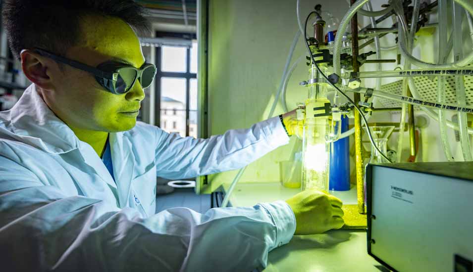 Chemiker mit Schutzbrille in einem Labor leuchtet einen Kolben mit einer Lampe an