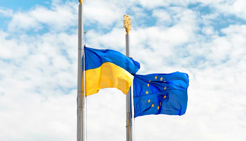 Flaggen der Ukraine und Europa an Fahnenmasten vor blaubewölktem Himmel