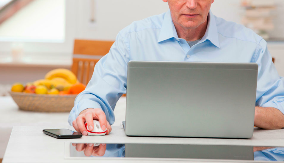 Mann arbeitet am laptop im Homeoffice, im Hintergrund steht ein Obstkorb.