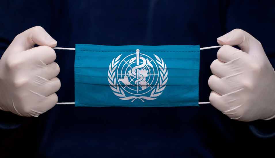 Person mit Handschuhen hält eine medizinische Gesichtsmaske mit der Flagge der Weltgesundheitsorganisation (WHO).