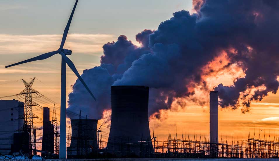Windkraftrad vor dampfendem Kohlekraftwerk bei Sonnenuntergang in Nordrhein-Westfalen