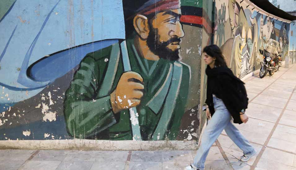 Junge Frau ohne Kopftuch läuft in Teheran an einer Mauer mit einem Wandbild entlang