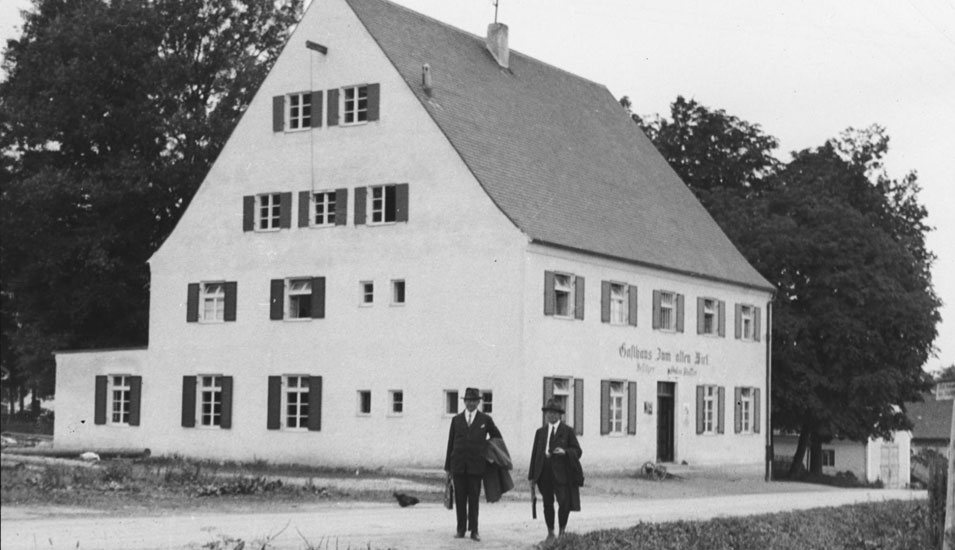 Dieses Bild zeigt eines der Häuser, die der Bayerische Landesverein für Heimatpflege e.V. zuordnen möchte, vor dem Haus stehen zwei Männer.