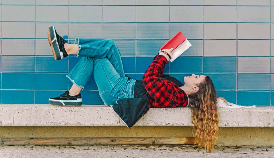 junge Frau liegt auf einer Bank und liest ein Buch